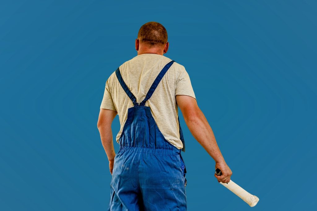 Professional house painter in blue overalls holding paint brush against blue sky background PITTSBURGH
