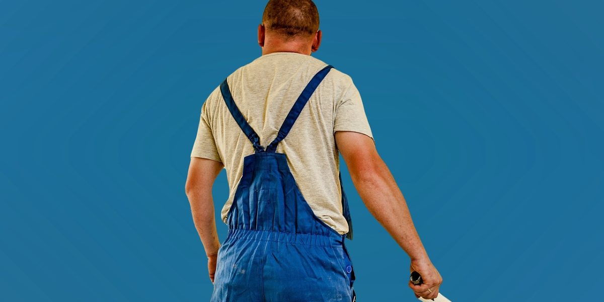 Professional house painter in blue overalls holding paint brush against blue sky background PITTSBURGH