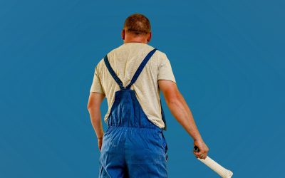 Professional house painter in blue overalls holding paint brush against blue sky background PITTSBURGH