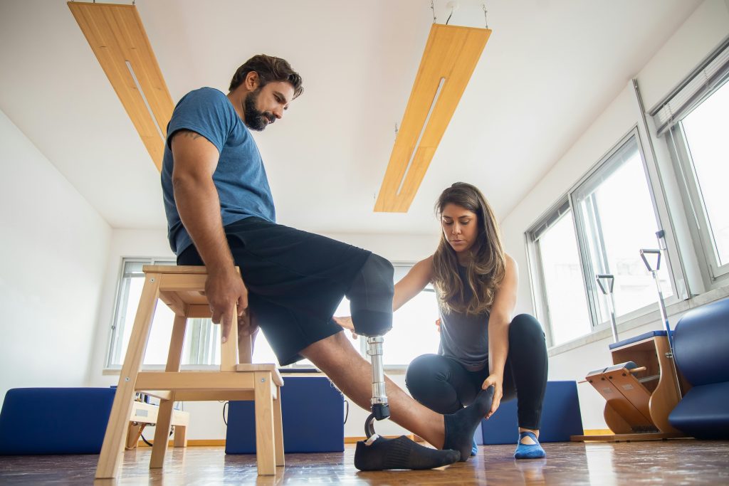 Physical therapist assisting a man with a prosthetic leg during rehabilitation exercises.
