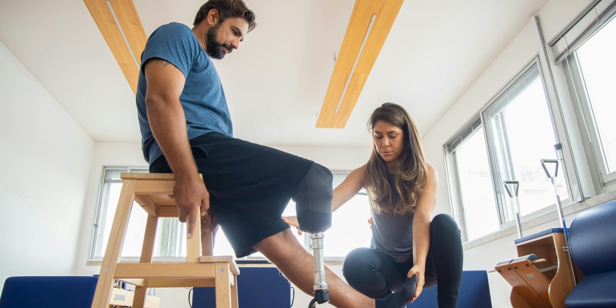 Physical therapist assisting a man with a prosthetic leg during rehabilitation exercises.