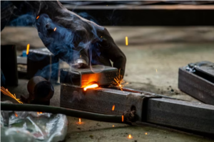 Worker performing precision investment casting process pouring molten metal into ceramic mold with sparks flying in industrial foundry