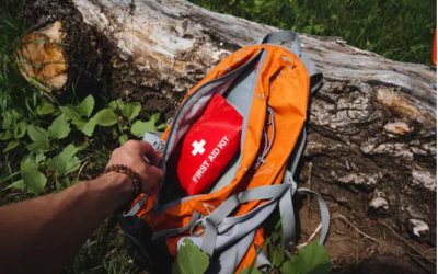 Hand Reaching For Red First Aid Kit Pouch Inside Orange Hiking Backpack On Forest Trail With Fallen Log