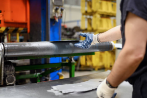 Worker inspecting metal tube during sheet metal fabrication process in industrial manufacturing facility