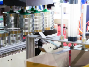 Automated tin can sealing machine applying lids to multiple metal cans on a production line.
