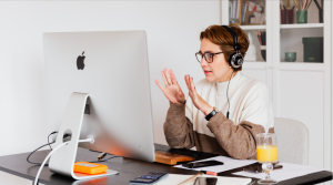 Professional woman with headphones participating in an online video meeting while working at a desktop computer in a home office.
