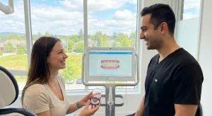 How Invisalign Treatment Creates Picture-Perfect Smiles Guided by Orthodontists in Surrey 1 A smiling patient and orthodontist discussing Invisalign treatment in a modern Surrey clinic, with the woman holding clear aligners and digital teeth scans visible on a monitor.