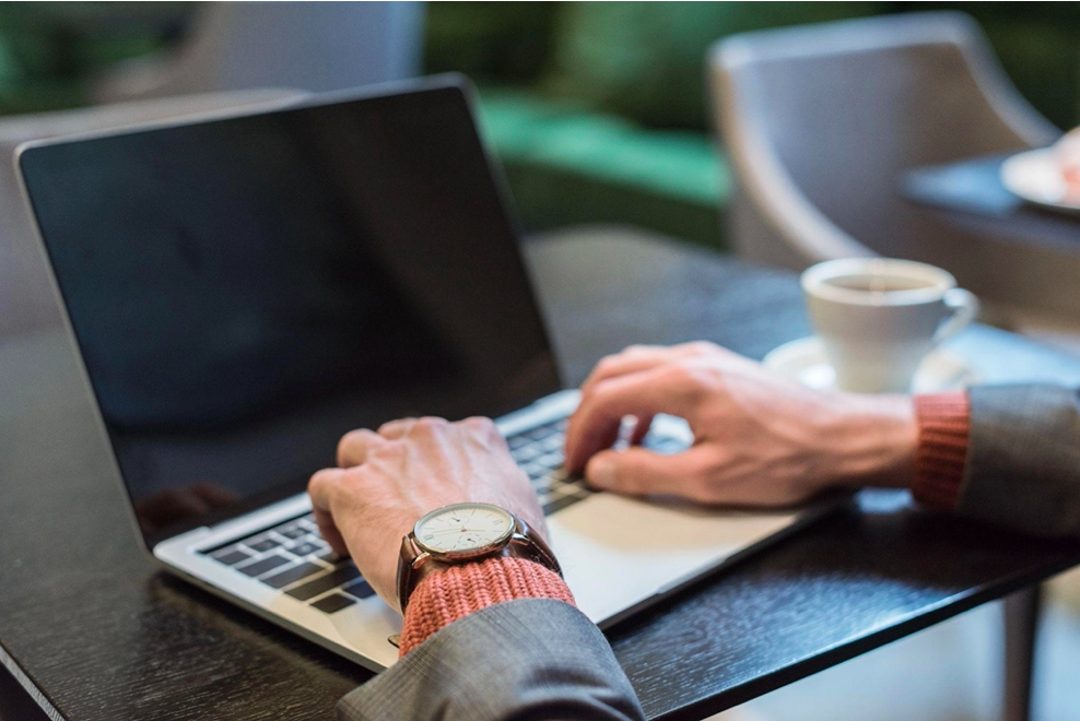 Person typing on laptop at coffee shop with watch on wrist and coffee cup nearby