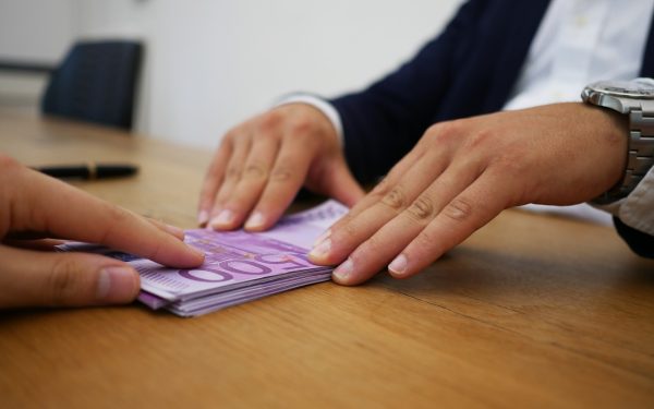 Two People Exchanging A Stack Of Euro Banknotes On A Wooden Table During A Loan Transaction
