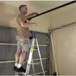 The Perks Of Upgrading Your Garage Door Technology 19 Technician Standing On A Ladder Inspecting The Overhead Garage Door Track And Hardware Inside A Garage