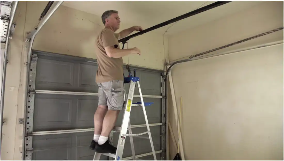 The Perks Of Upgrading Your Garage Door Technology 1 Technician Standing On A Ladder Inspecting The Overhead Garage Door Track And Hardware Inside A Garage